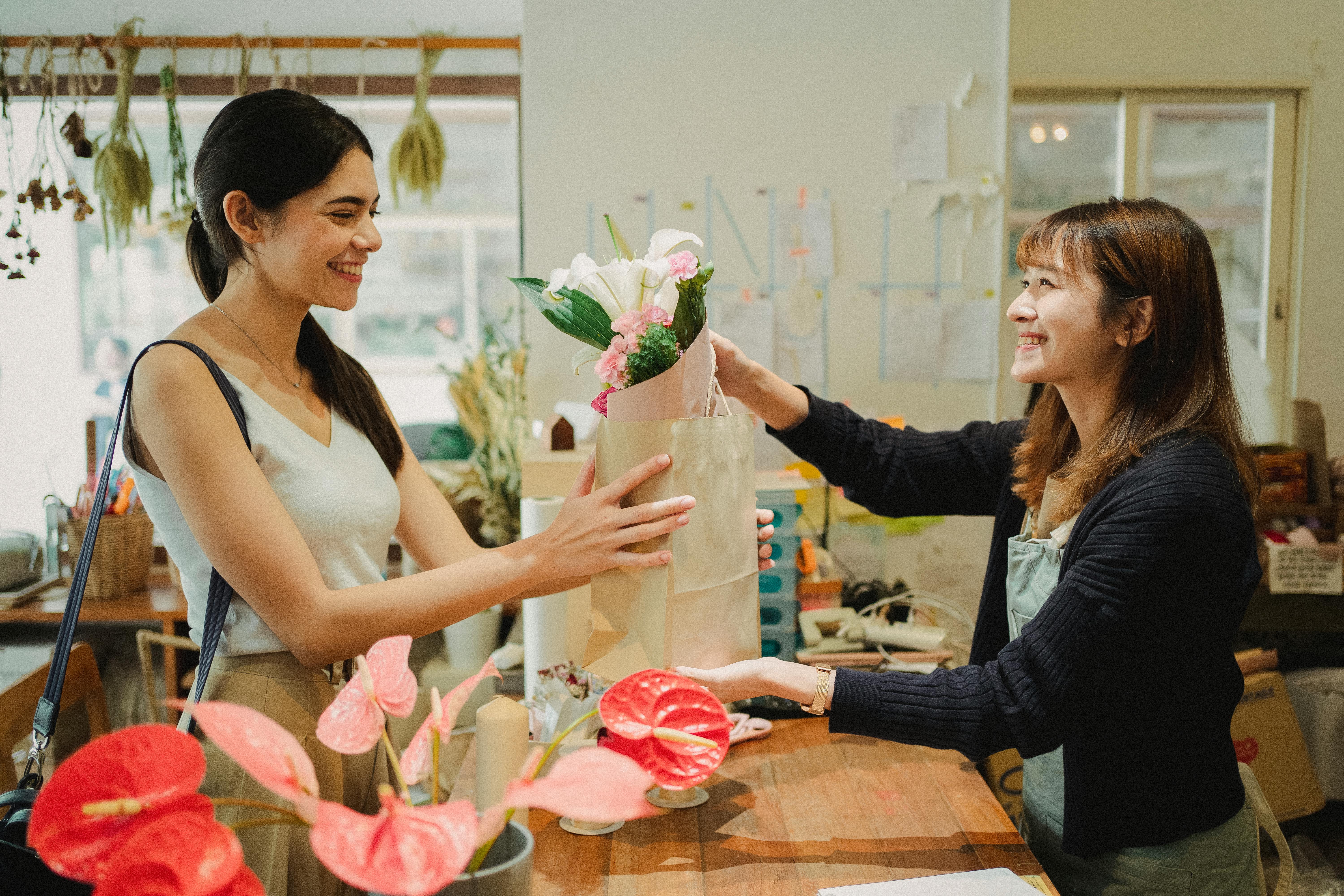 花屋の店員が外国人のお客様に笑顔で商品を手渡している様子